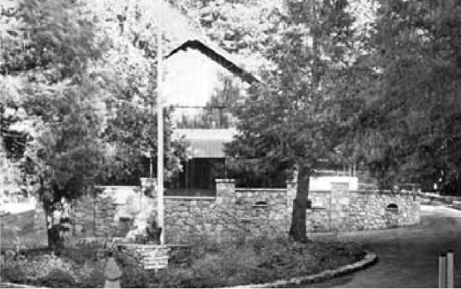 Archival photograph from about 1917 showing the newly built granite wall, a flagpole and the lodge behind it.